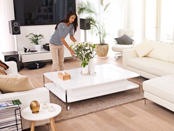 Woman arranging flowers on a white coffee table in a bright, modern living room.