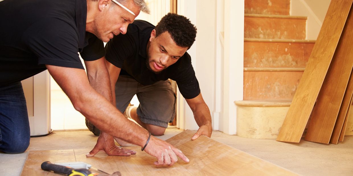 Two men installing wooden flooring together indoors.