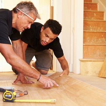 Two men installing wooden flooring, focusing on alignment.