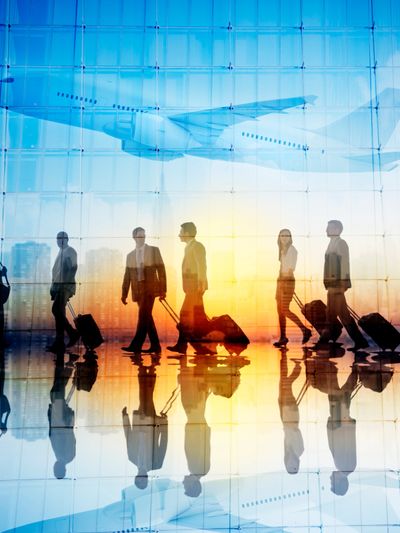 Business travelers walking with luggage at an airport during sunset with a plane overhead.