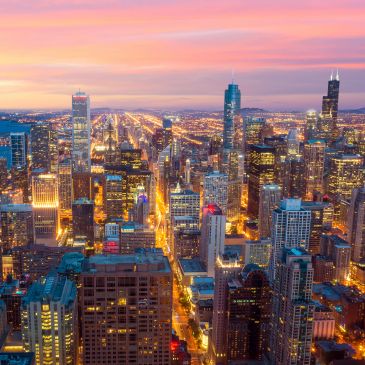 City skyline at sunset with illuminated buildings and streets.