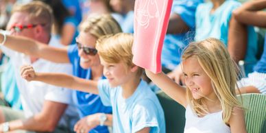Excited kids and adults cheering at a sports event with a foam finger.