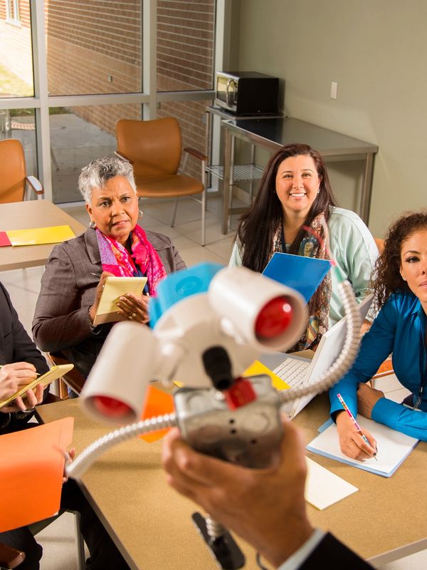 A group of women attentively listening to a person demonstrating a device in a meeting room.