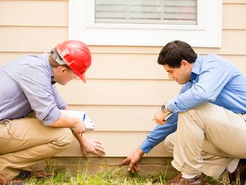 Two men inspecting a house's foundation.