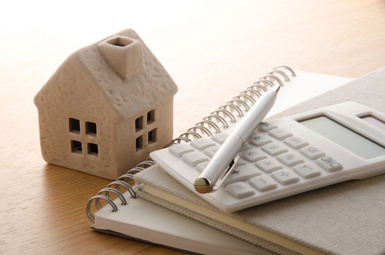 A miniature house, calculator, pen, and notebooks on a wooden table.
