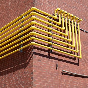 Yellow pipes neatly aligned along a red brick wall corner.
