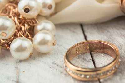 two wedding bands with a necklace of pearls on white wood.