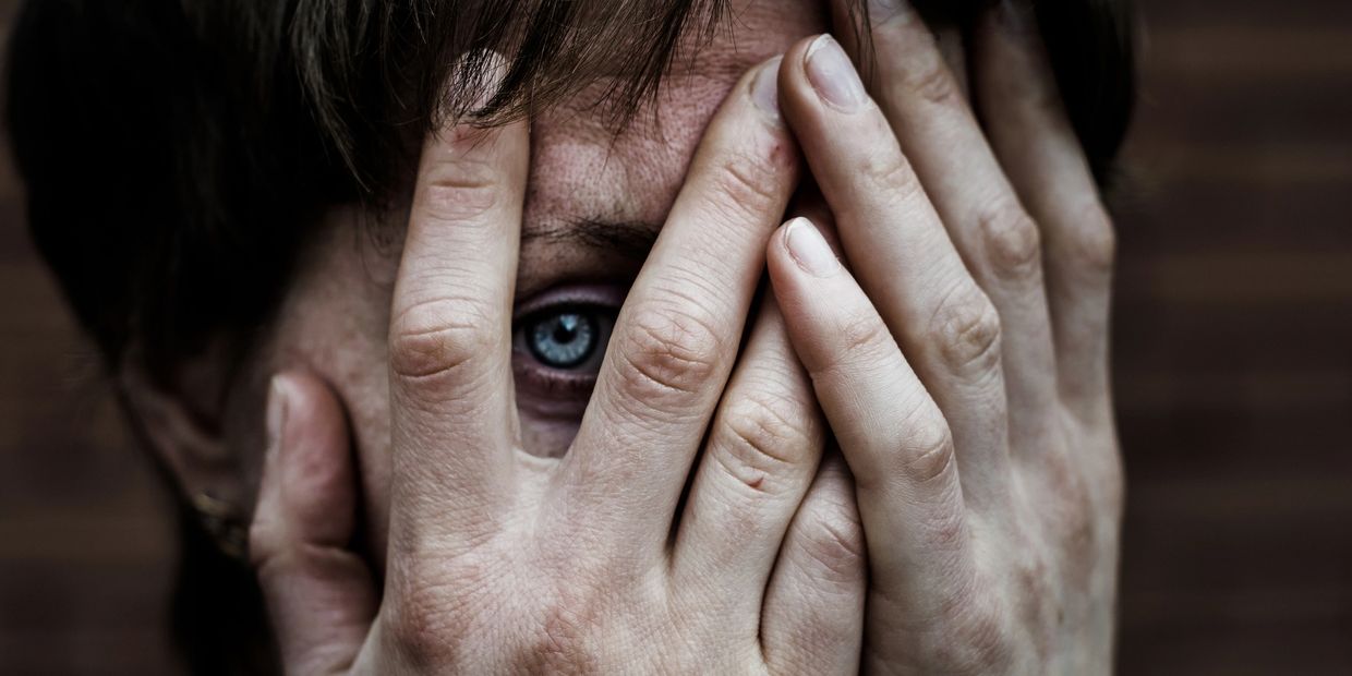 Person peeking through fingers with a worried expression.