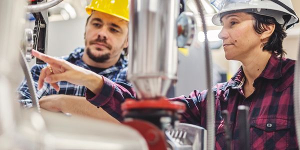 Two engineers inspecting machinery, wearing safety helmets and plaid shirts.