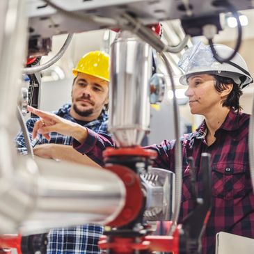 Two engineers inspecting industrial machinery, wearing safety helmets.
