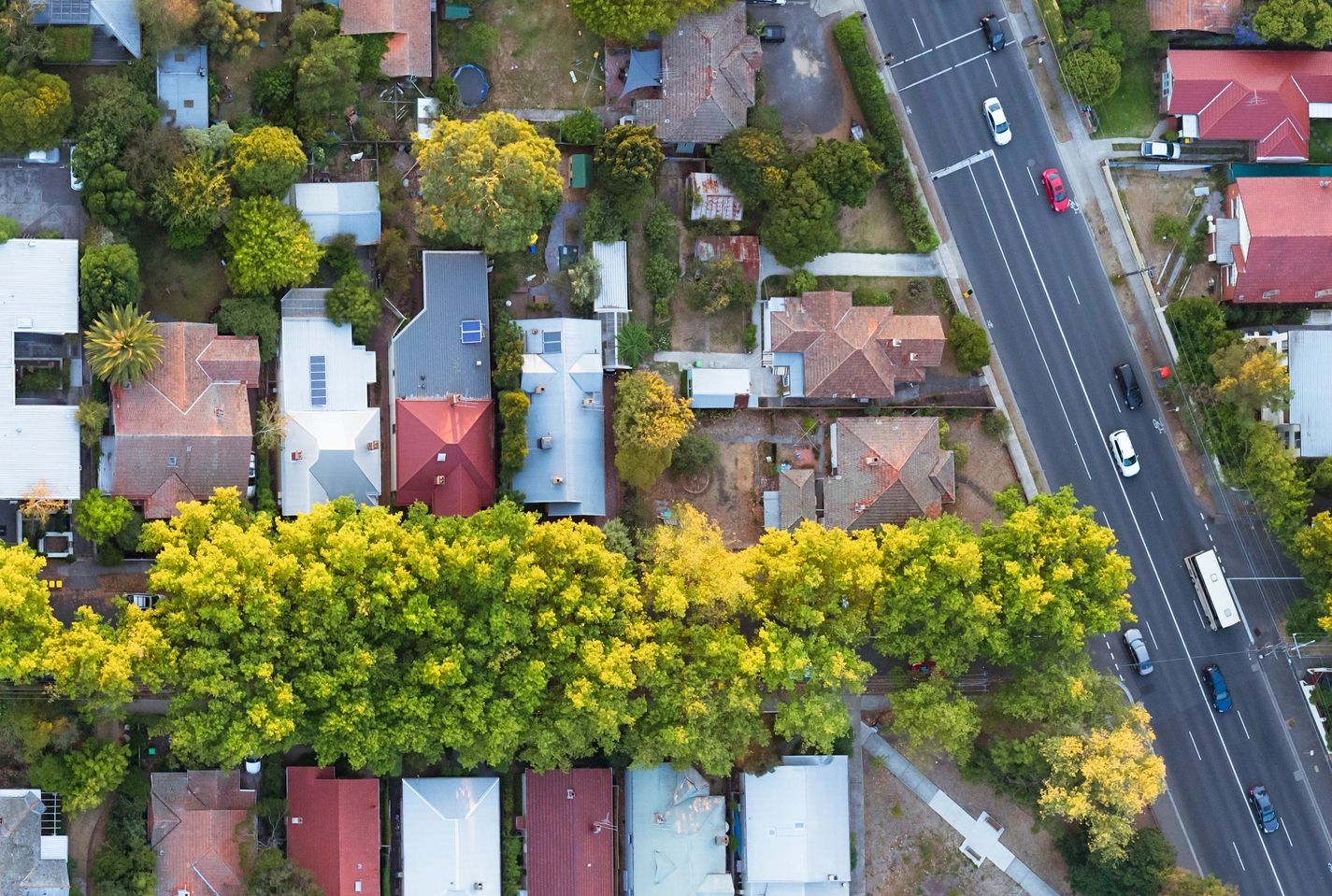 Aerial view of a residential neighborhood with houses, trees, and a busy road.