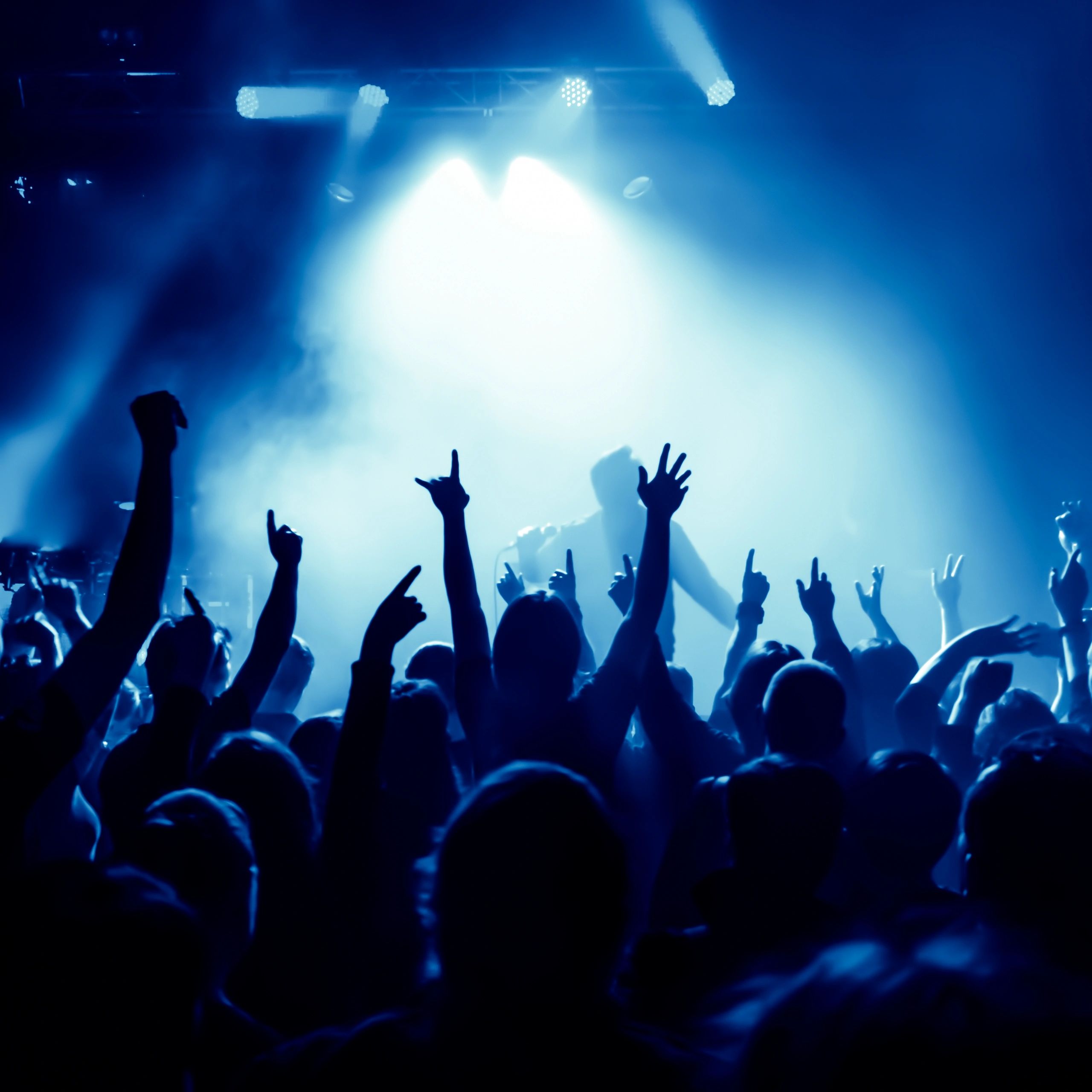 Crowd at a concert with hands raised under blue stage lights.