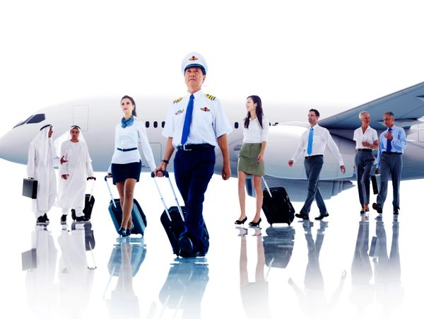 Airline crew and business travelers walking with luggage near an airplane.