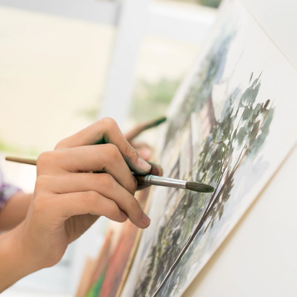 Close-up of a person painting a detailed tree on canvas with a brush.