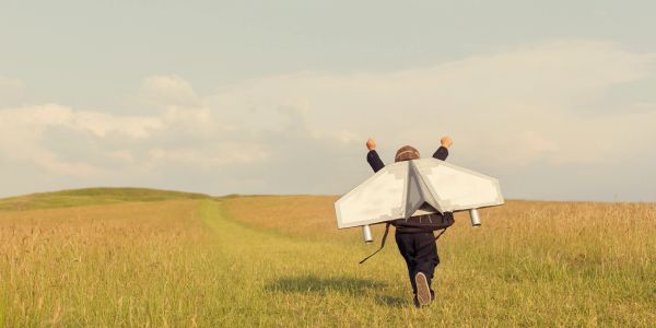 Child running with a cardboard jetpack in a field.