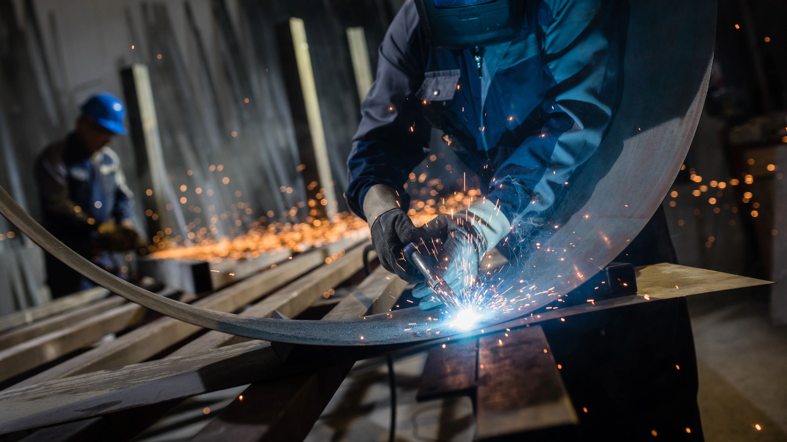 Worker welding metal with sparks flying in workshop.