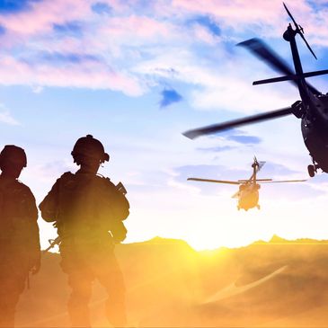 Soldiers standing at sunset with helicopters flying.