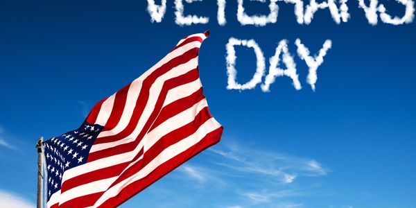 American flag waving under a sky with 'Veterans Day' written in clouds.