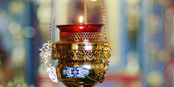 Lit ornate hanging oil lamp with red glass.