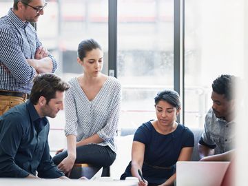 A diverse team collaborates on a project around a laptop.