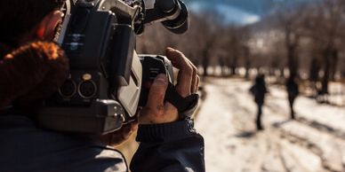A cameraman filming a person walking on a snowy path.