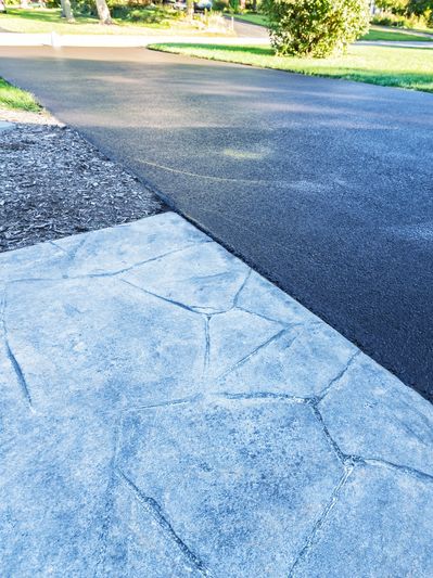 A driveway with a textured concrete sidewalk beside it on a sunny day.