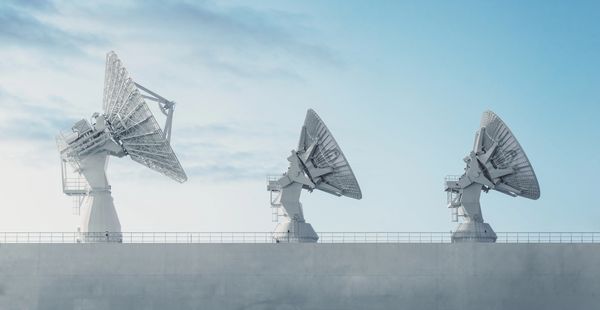 Three large satellite dishes against a blue sky.