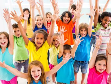 Happy children raising their hands and smiling brightly indoors.