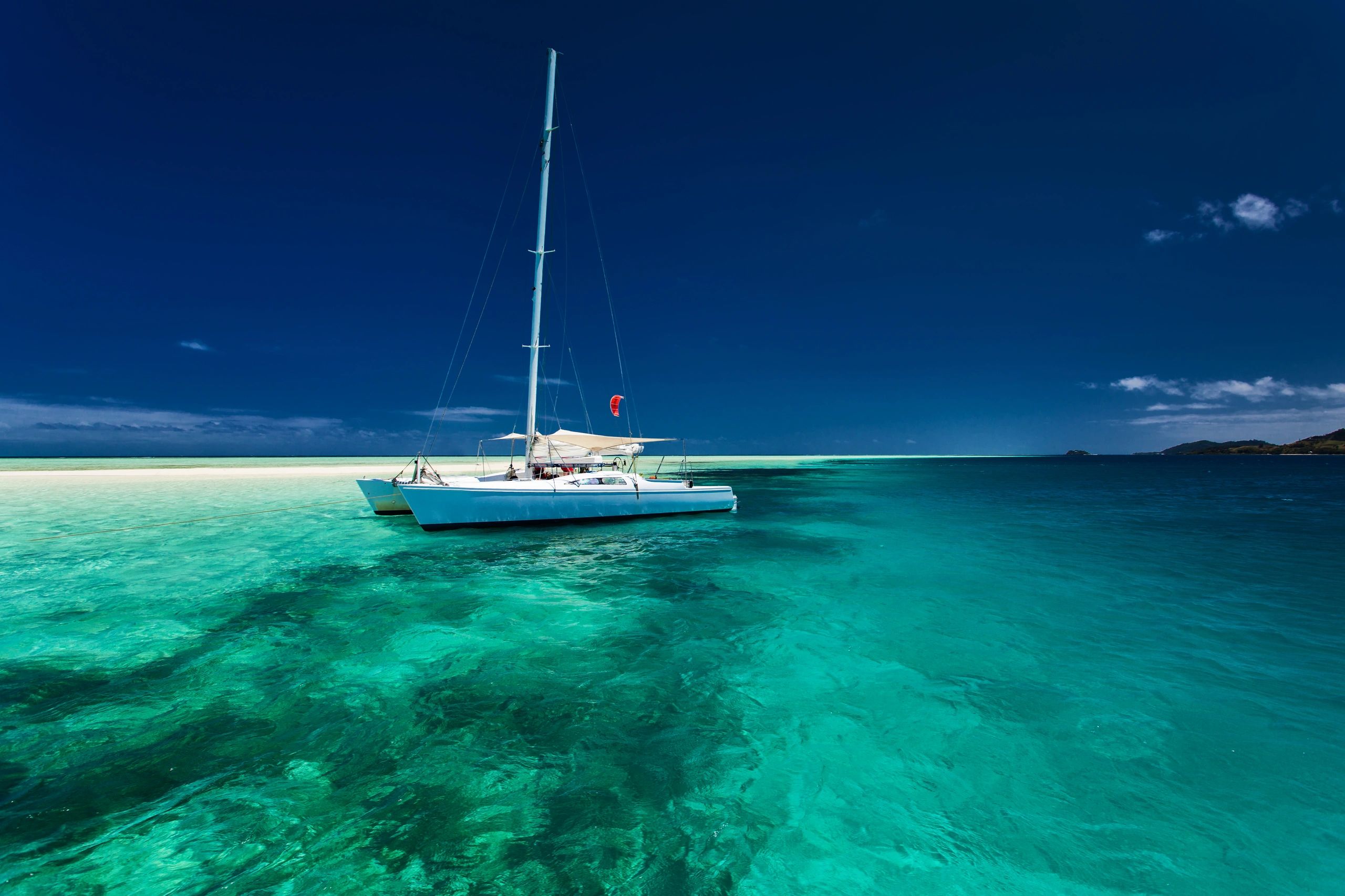 Sailing yacht anchored in clear turquoise water beside a white sandbar and tropical island.