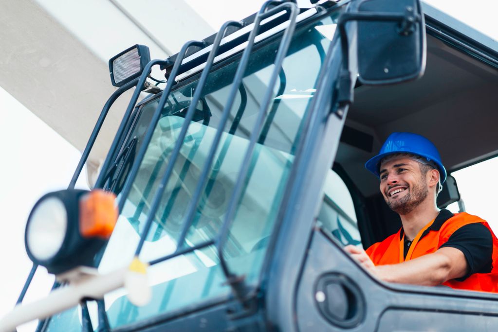 Smiling construction worker operating heavy machinery wearing safety gear.