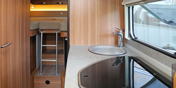 Compact RV kitchen with sink, stove, and ladder to sleeping area.