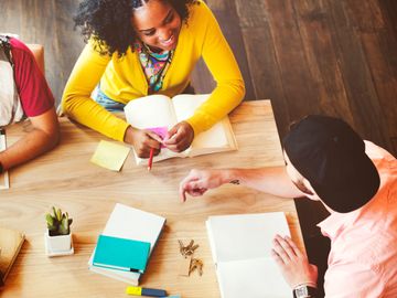 Young people studying and discussing ideas around a wooden table.