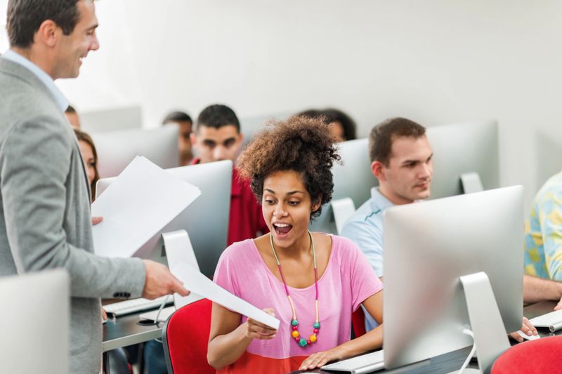 Happy African American student receiving test results from professor in computer lab.