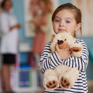 A young girl hugging a teddy bear in a medical setting.