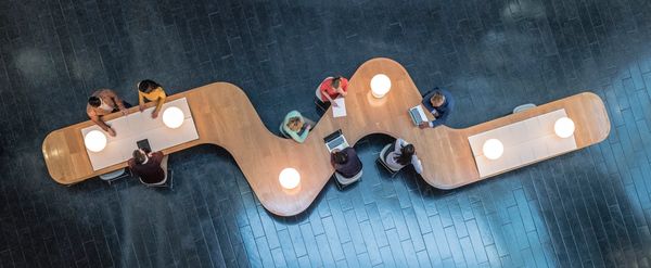 Overhead view of people working and collaborating at a uniquely shaped wooden table.