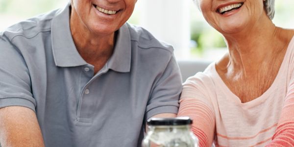 Happy elderly couple showing a jar labeled savings filled with money.