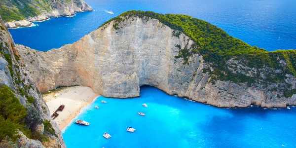 A stunning beach cove with turquoise water and boats near towering cliffs.