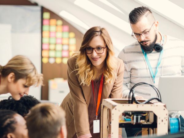 A team collaborates around a 3D printer in a modern workspace.
