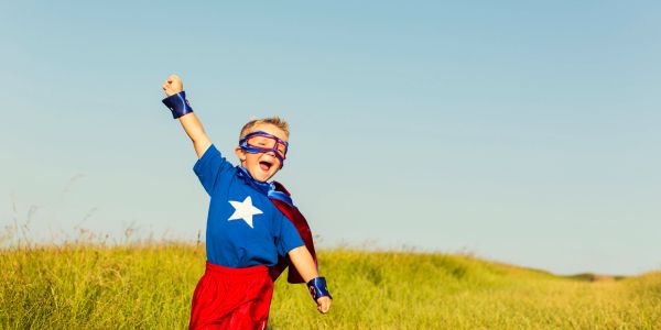 Child dressed as superhero in a field.