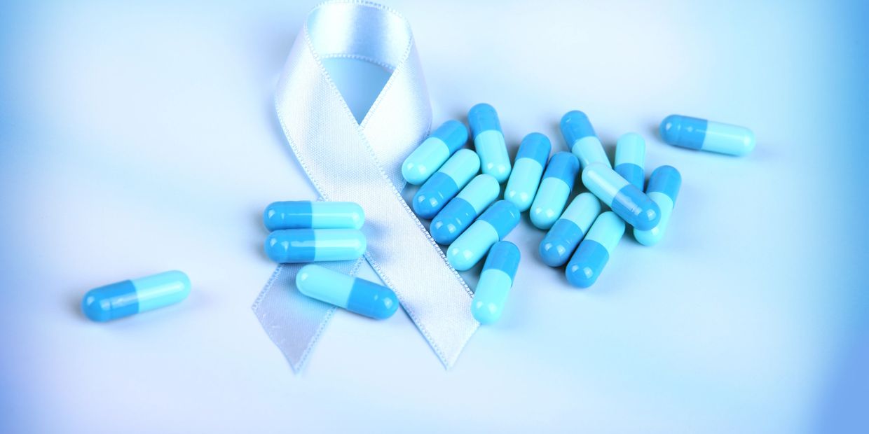Blue capsules scattered near a white awareness ribbon on a light background.