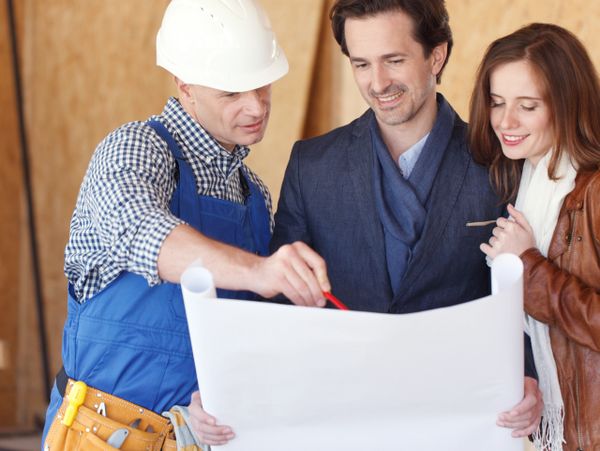 Construction worker explaining blueprint to a couple in a building under construction.