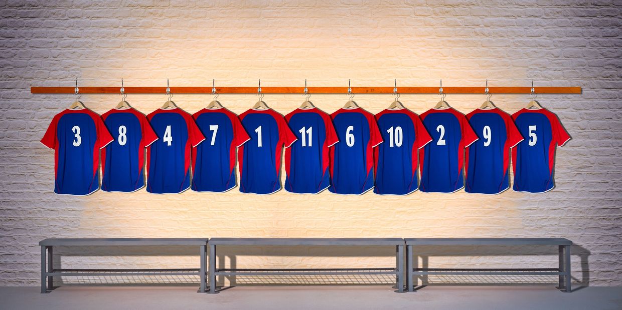 Row of numbered sports jerseys hanging on a wall above benches.