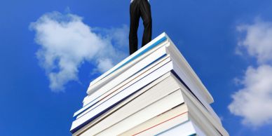 Person standing atop a tall stack of books reaching the sky.