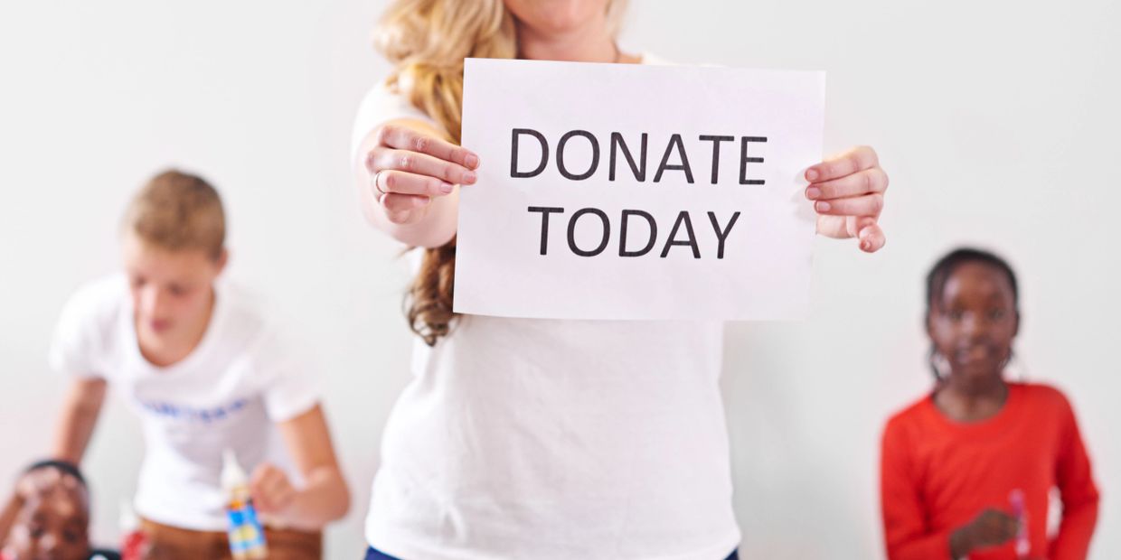 Woman holding a sign that says "DONATE TODAY" with children in the background.