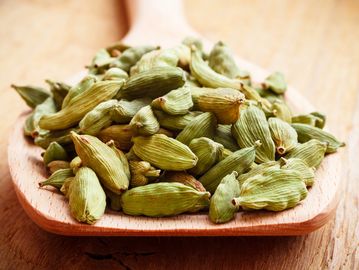 Green cardamom pods on a wooden spoon.