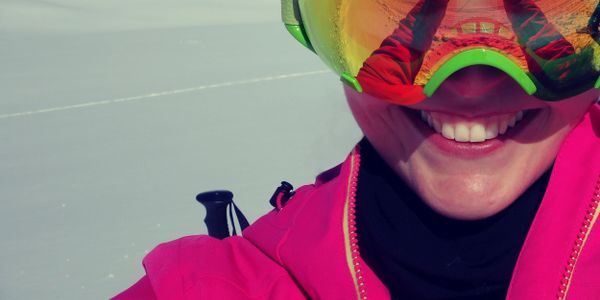 Smiling skier in bright pink gear on snowy slopes.