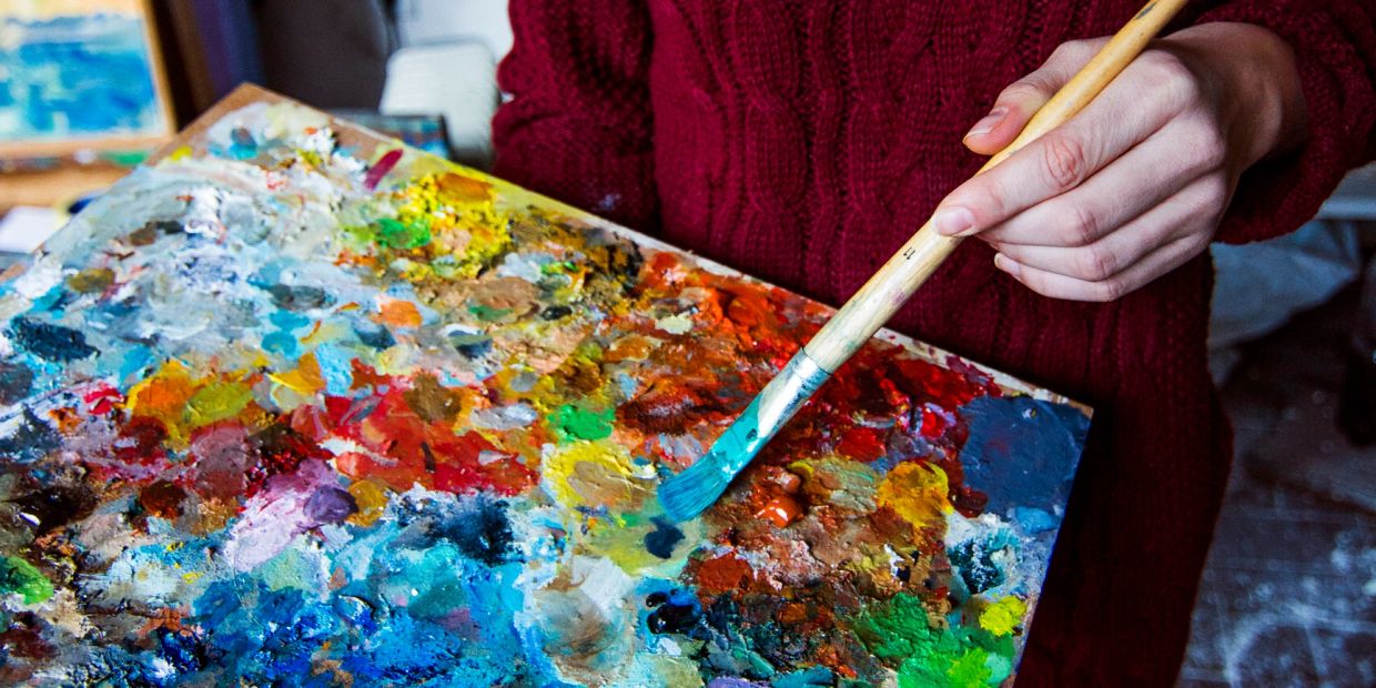 Person holding a paintbrush over a colorful artist's palette.