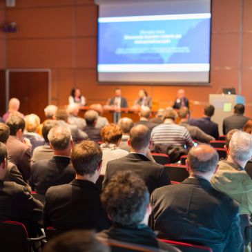 Audience attending a conference with speakers at the front.
