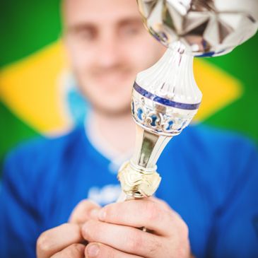 Person holding a trophy in front of a Brazilian flag.