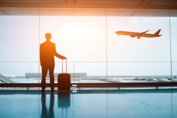 Businessman with suitcase watching plane take off at airport.